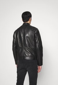 Zwarte leren jack met een gladde textuur, voorzien van een staande kraag en naaddetails. De achterkant toont een schone, aansluitende silhouet.