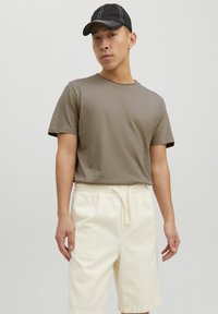 Camiseta de manga corta marrón con cuello redondo, combinada con pantalones cortos de color crema que cuentan con una cintura elástica y cordón. Gorra negra con costuras blancas.