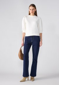 White puff-sleeve top paired with dark blue flared jeans, featuring a brown handbag and beige pointed toe heels. Smooth textures, modern design.
