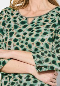 Tunic verde con stampa leopardata realizzata in un tessuto morbido e leggero. Presenta un collo rotondo con un piccolo foro a forma di chiave e maniche a tre quarti.