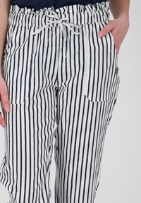 Pruhované lněné kalhoty s vodorovnými námořnickými a bílými pruhy, elastickým pasem se šňůrkou a dvěma bočními kapsami.