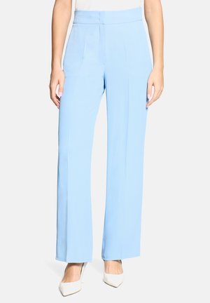 Pantalon large bleu clair en tissu lisse, avec une taille haute et des plis devant, assorti à des talons blancs à bout pointu.