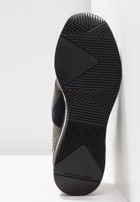 Zwarte en gouden sneakerzool met gestructureerd rubber, voorzien van een geometrisch patroon, gladde zwarte accenten en merktekening op de hak.