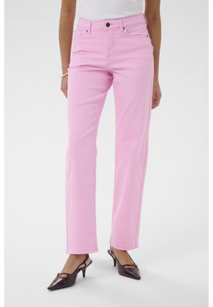 Femme portant un jean rose droit taille haute avec poches avant et des chaussures à talons slingback bordeaux foncé, sur un fond uni.