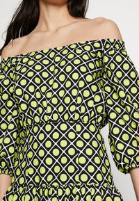 Schwarzes und limettengrünes, schulterfreies Kleid mit geometrischem Muster aus Kreisen und Rauten, gerafften Ärmeln und einem Rüschensaum.