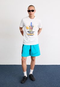 White Nike t-shirt with colorful drink graphic, paired with turquoise shorts featuring black accents and logo. Black sneakers and white socks.