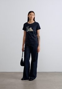 Μαύρο βαμβακερό μπλουζάκι με εμπρός γραφικό σχέδιο που απεικονίζει έναν σκύλο, βάζο και φυτό. Συνδυασμένο με σκούρο τζιν παντελόνι φαρδιάς γραμμής και μαύρη τσάντα.