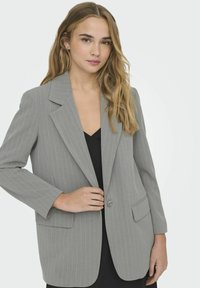 Blazer gris a rayas con solapa muesca, cierre de un botón y dos bolsillos frontales. La tela parece suave y bien ajustada.