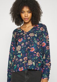 Blusa de manga longa floral em azul-marinho, com padrões vibrantes e multicoloridos de flores e folhas, design em V e corte solto.