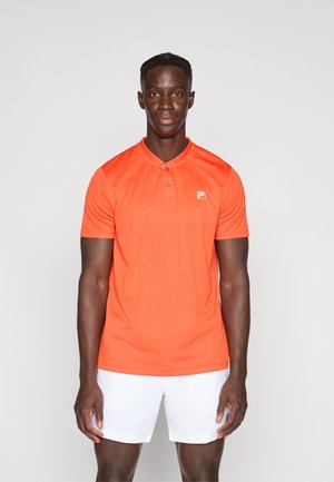 Helles orangefarbenes Poloshirt mit strukturiertem Design, kurzen Ärmeln und einem geknöpften Kragen, ausgestattet mit einem kleinen Logo auf der Brust. Kombiniert mit weißen Shorts.