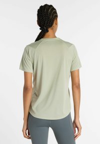 Light green athletic shirt with short sleeves, textured fabric, and a rounded hem, paired with gray leggings. No visible logos or patterns.