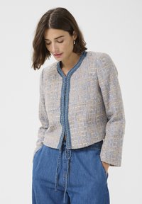 Fitted jacket in textured beige and blue fabric, featuring a round neck, decorative blue trim, and a cropped silhouette.