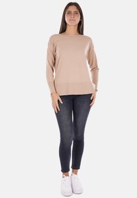 Maglione beige a maniche lunghe con scollo rotondo, vestibilità comoda e orlo a coste, abbinato a jeans skinny scuri e sneakers bianche.