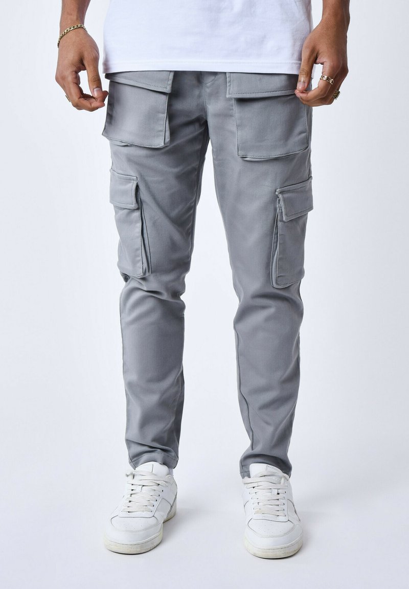 Pantaloni cargo grigio con multiple tasche frontali, fit slim e tessuto leggero. Abbinati a sneaker bianche.