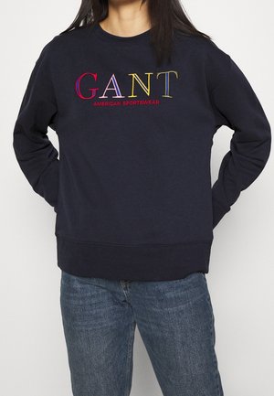 Felpa blu navy con scollatura tonda, polsini e orlo a coste. Presenta il testo ricamato multicolore "GANT AMERICAN SPORTSWEAR" sul davanti.