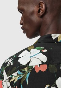 Koszula z krótkim rękawem w kwiatowy wzór na czarnym tle z dużymi białymi i czerwonymi kwiatami, kołnierzykiem oraz gładką, lekką tkaniną.