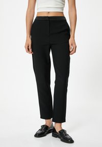 Zwarte gepaste broeken met een gladde textuur en slim fit, voorzien van een tailleband en zakken, aangevuld met glanzende zwarte instappers.