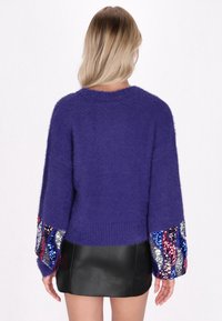 Maglione viola peloso con maniche ampie, caratterizzato da paillettes multicolori sui polsini. Il tessuto ha una consistenza morbida e una vestibilità comoda.