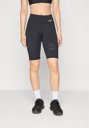 Svart sykkelshorts med høy midje og et teksturert panel med tre horisontale striper. Kombinert med svarte treningssko og hvite sokker.