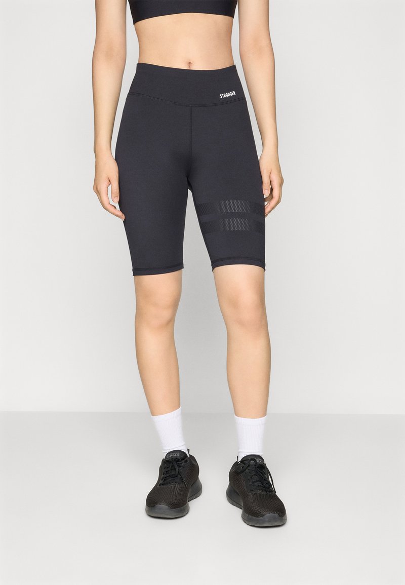 Schwarze Radlerhosen mit hoher Taille und einem strukturierten Einsatz mit drei horizontalen Streifen. Kombiniert mit schwarzen Sportschuhen und weißen Socken.