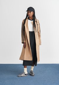 Ruskeanrakotakki mustilla raidoilla, valkoinen toppi, musta hame ja harmaat kengät valkoisten sukkien kanssa. Musta hattu ja letit täydentävät asun.