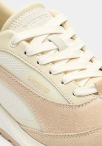 Zapato deportivo beige que combina cuero liso y malla, con cordones redondos y una entresuela texturizada con un detalle de logo discreto.