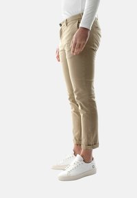 Chinos beige con una vestibilità slim, orli arrotolati e due tasche anteriori, abbinati a sneakers bianche con dettagli perforati e lacci.