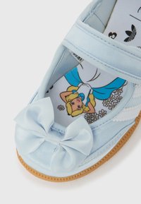 Ljusblå småbarnssko med en sidenrosett på toppen och en innersula med tryck av en flicka i en blå och vit klänning med blommor.
