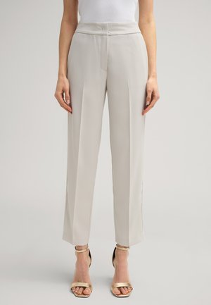 Pantaloni beige chiaro su misura con vita alta, caratterizzati da pieghe frontali e un tessuto liscio. Abbinati a sandali metallici con cinturini.