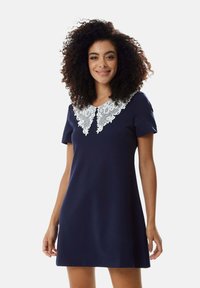 Navy blue dress with short sleeves, features a white lace collar with intricate patterns. Made from a smooth, stretchy fabric.