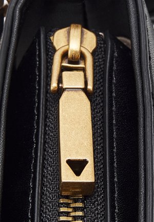 Close-up van een gouden ritstrekker op een zwarte stoffen ondergrond met zichtbare rits tanden en stiknaden.