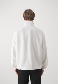 Chaqueta blanca ligera con cuello alto, puños elásticos y un corte relajado. Textura suave, diseño sencillo, adecuada para uso casual.