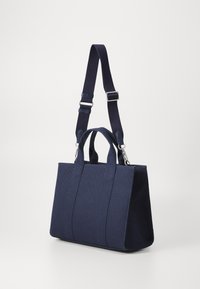 Navy blue canvas tote bag with two top handles and an adjustable shoulder strap, featuring a structured shape and visible stitching details.