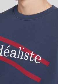 Sudadera de algodón azul marino con texto blanco en negrita que dice "délististe" y un acento rojo en diagonal debajo del texto. Cuello redondo.