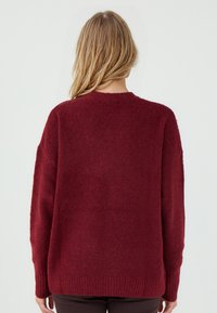 Burgundowa sweter z dzianiny z długimi rękawami i okrągłym dekoltem. Teksturowany, miękki materiał o luźnym kroju i ribbowe wykończenie u dołu.