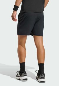 Čierne športové šortky s textúrovaným povrchom, s bočnými vreckami a uvoľneným strihom, skombinované s čiernymi ponožkami a čierno-bielymi teniskami.