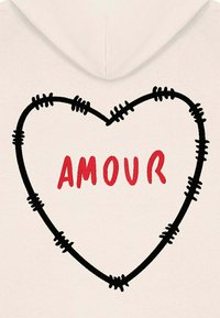 Sudadera de color crema con un contorno de corazón negro bordado, detalles de costura y la palabra "AMOUR" en letras rojas en negrita en el interior.