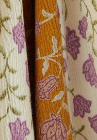 Tissu côtelé plié avec des motifs floraux en violet et vert sur fond de fleurs blanches et violettes avec des feuilles blanches sur fond jaune moutarde.