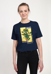 Tmavě modré tričko s grafickou potiskem Van Goghových "Slunečnic" a textem. Design zahrnuje žlutá pozadí a květinové vzory.