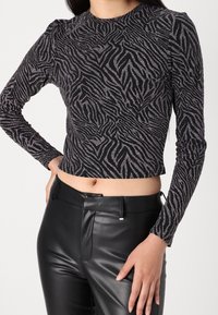 Musta pitkähiha toppi, jossa on striippikuosi metallinhohtoisessa hopeassa, ja se on tiukasti istuva sekä lyhythelmainen. Yhdistetty mustiin housuihin.