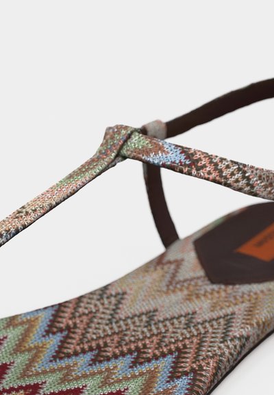 Κοντινή λήψη ενός σανδαλιού με σχέδιο και πολύχρωμους υφασμάτινους ιμάντες σε σχήμα ζιγκ ζαγκ και τετράγωνο σχεδιασμό στο μπροστινό μέρος, σε λευκό φόντο.