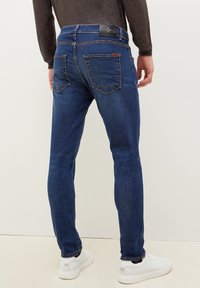Mörkblå, slim-fit jeans i denim med femfickorsdesign och subtil sömnad, bärs med vita sneakers.