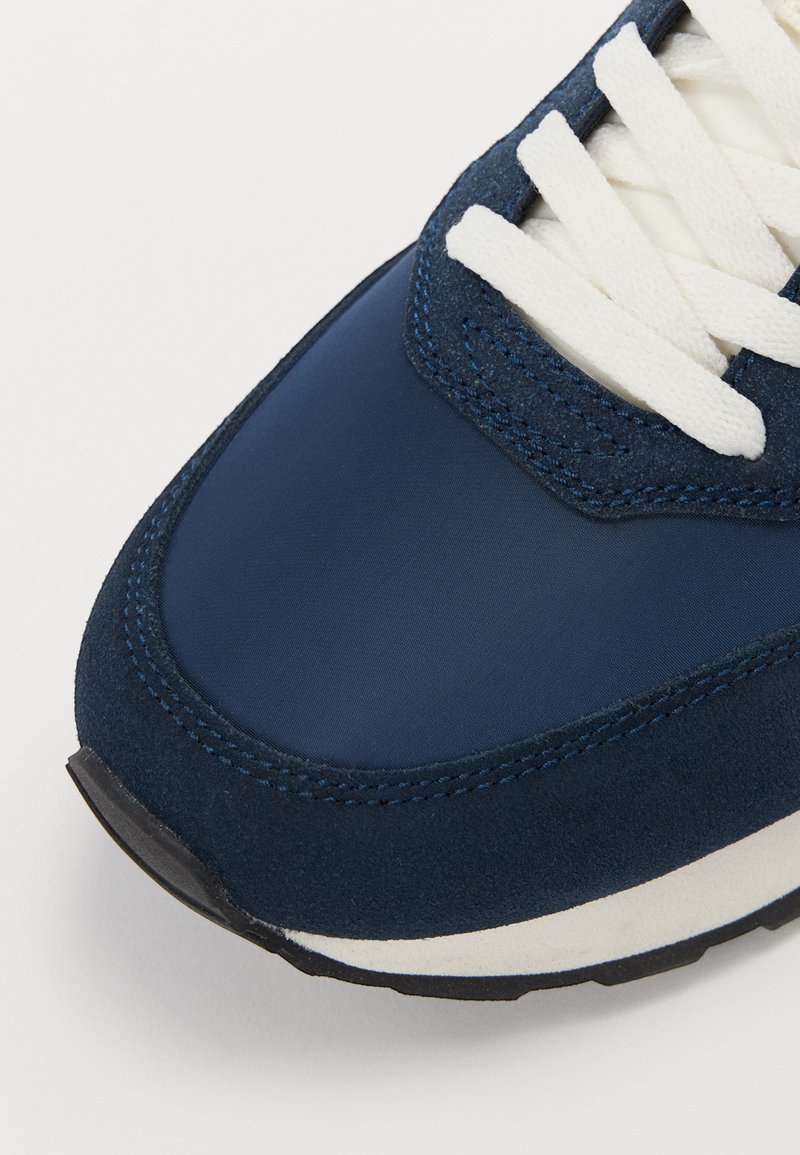 Scarpa sportiva blu navy con tomaia sintetica liscia, dettagli in suede, lacci bianchi e suola in gomma nera testurizzata.