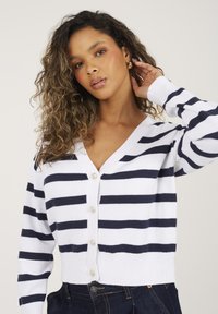 Ciemnoniebieski i biały sweter w paski wykonany z dzianiny, z dekoltem w serek, długimi rękawami i sześcioma guzikami z przodu.