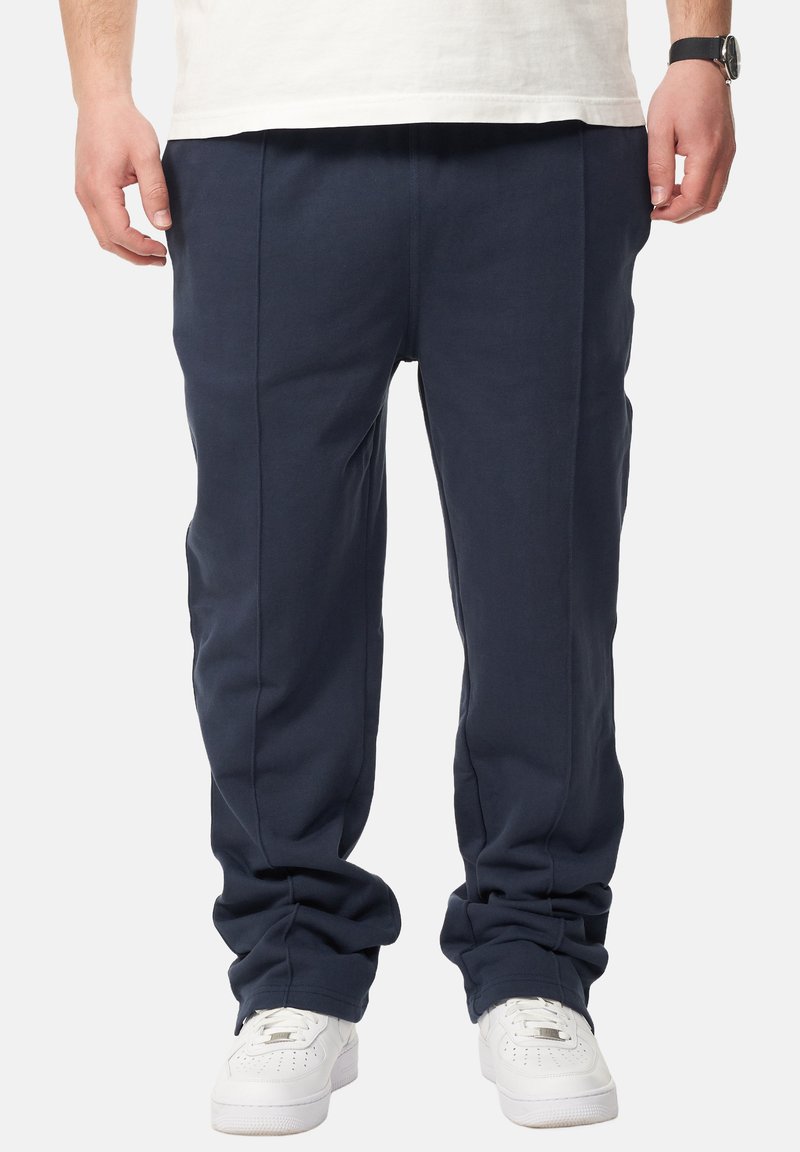 Marineblaue, lässig geschnittene Hose aus weichem Material mit glatter Textur, mit vorderen Falten und elastischem Bund. Getragen mit weißen Sneakers.