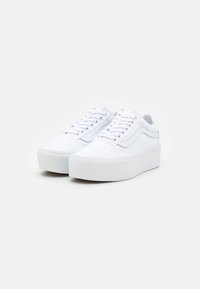 White canvas sneakers with a platform sole, featuring round laces, a side stripe, and textured rubber outsole. No distinct patterns or accents.