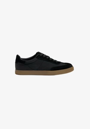 Scarpa da ginnastica nera con una texture liscia e scamosciata, design low-top, suola piatta in gomma marrone e chiusura con lacci standard.