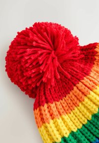 Strikket vinterhat med en stor rød pom-pom, der har vandrette striber i rød, orange, gul og grøn garn på en hvid baggrund.