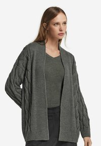 Grå cardigan med kabelstickad textur och ribbade kanter, öppen framsida, bärs över en matchande V-ringad topp, tillsammans med mörka byxor.