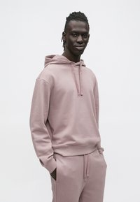 Prachovozvíćová ružová mikina z mäkkej látky, s kapucňou na šnúrku a rebrovanými manžetami. V páre s nohavicami v zodpovedajúcej farbe, s voľnejším strihom.